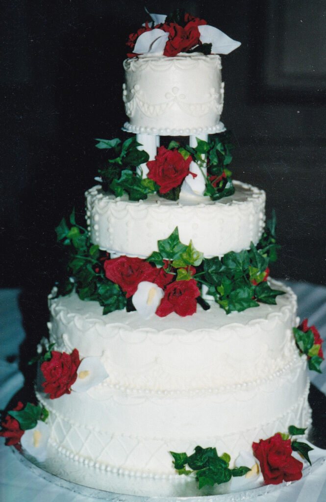 tiered wedding cake with piped designs and red and green flowers and leaves between the tiers