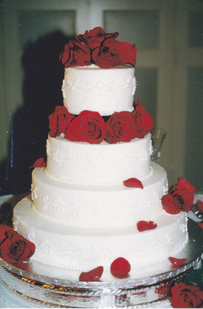 white buttercream wedding cake with piping and fresh red roses in pillars