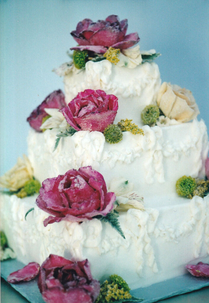 white square wedding cake with pped ruffles and sugared roses