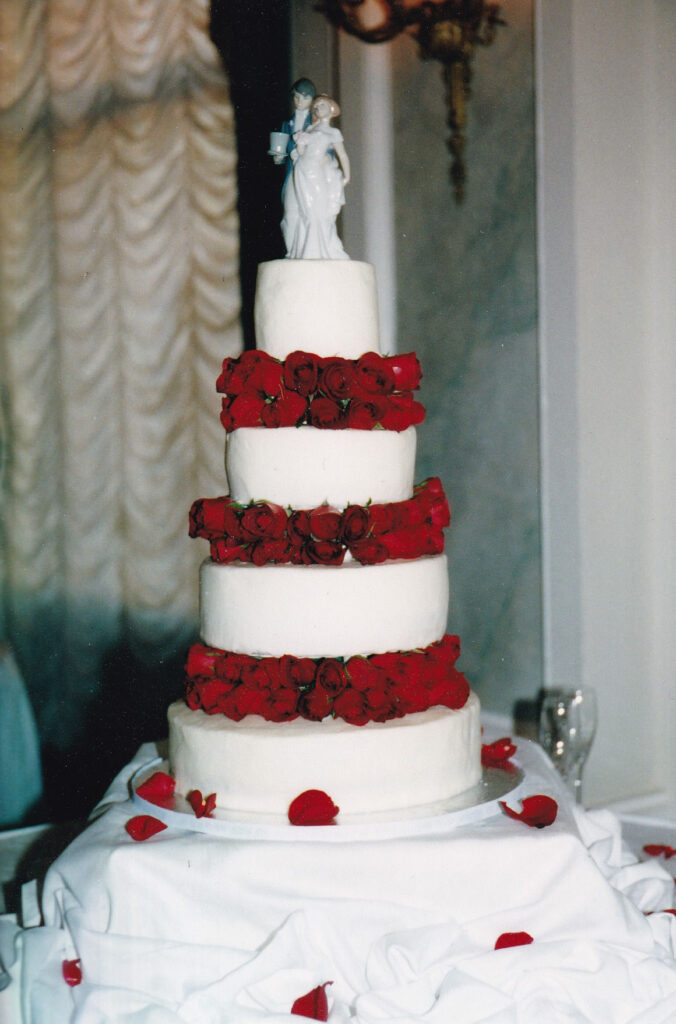 white wedding cake with fresh red roses between the tiers