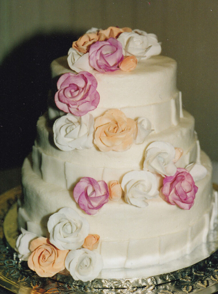 white wedding cake with pink and orange gumpaste roses and white pleats