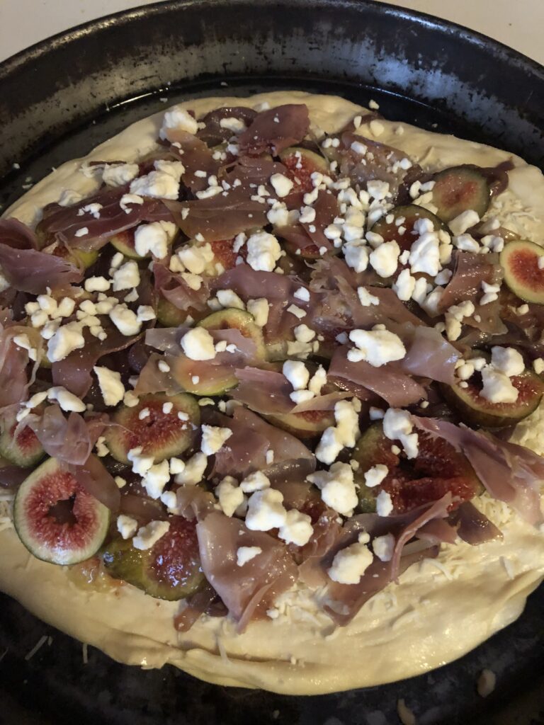 pizza dough in a pan with onions, feta, and figs on it