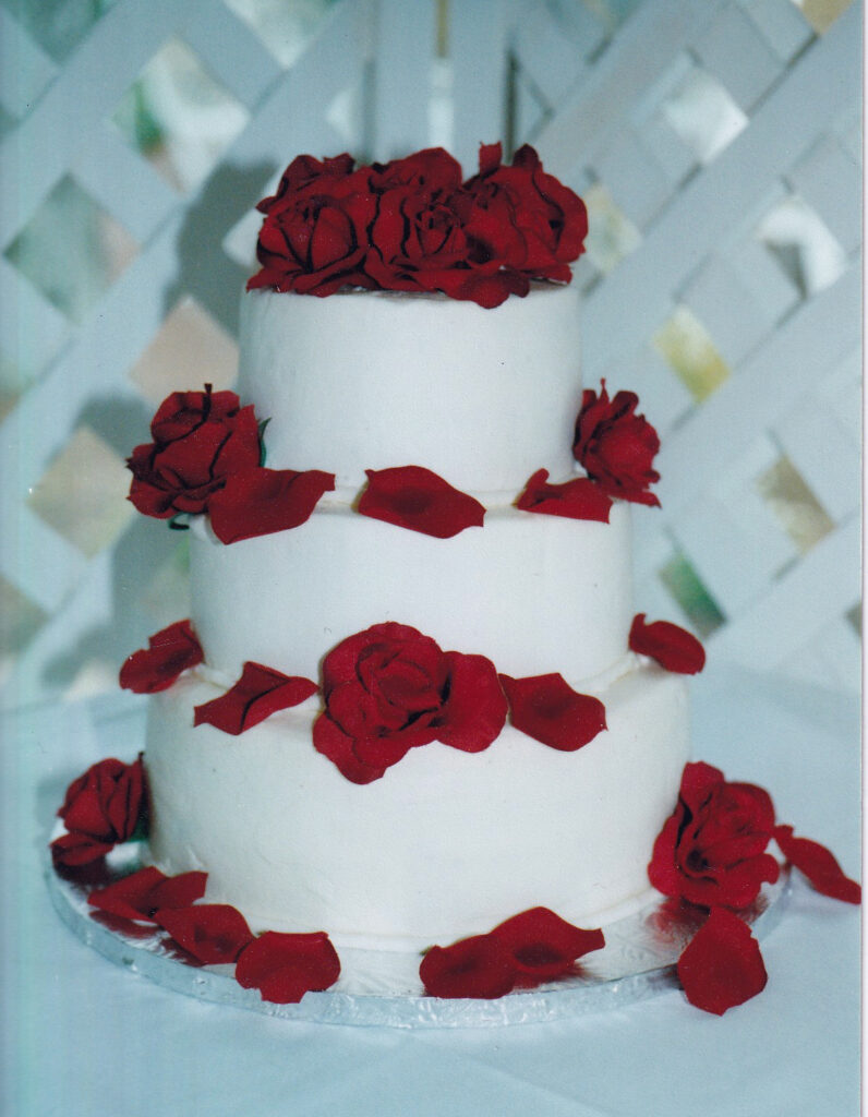 plain white wedding cake with fresh red roses on the tiers