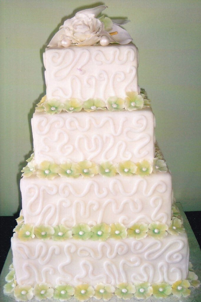 square wedding cake with green hydrangeas and scrollwork piped tiers