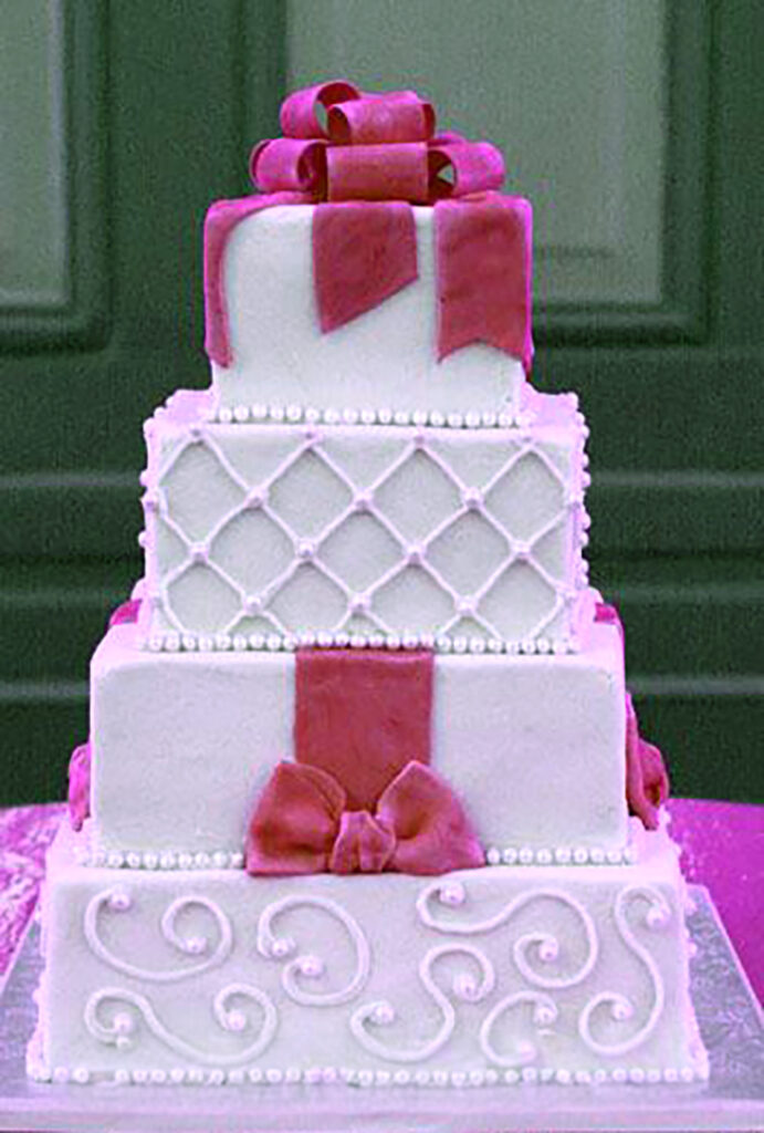 pink and white square tiers wedding cake with bow topper
