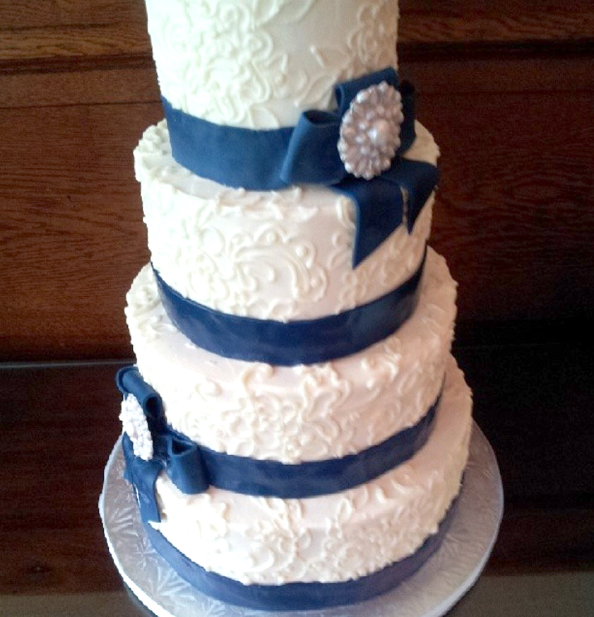 piped lace wedding cake with dark blue bands and bows and gumpaste brooches
