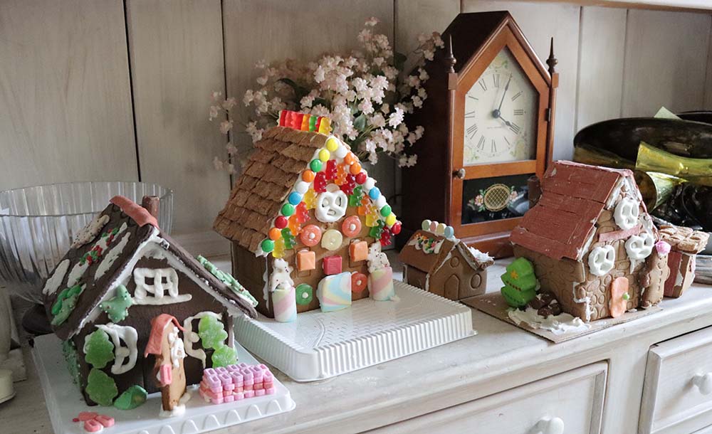 gingerbread houses on a shelf with a clock and vase of flowers